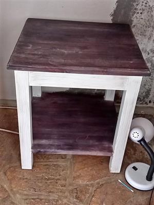 Wooden farmhouse-style side table with a dark-stained top and whitewashed legs.