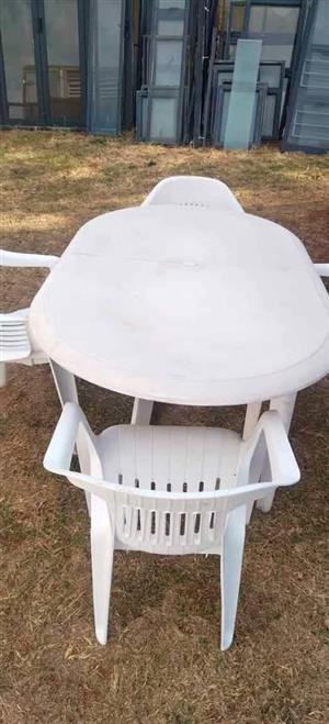 White outdoor patio table with 4 matching plastic armchairs...