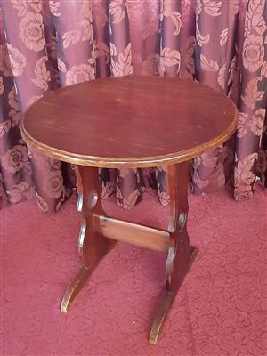 Round wooden occasional table, shaped trestle supports, connecting stretcher.